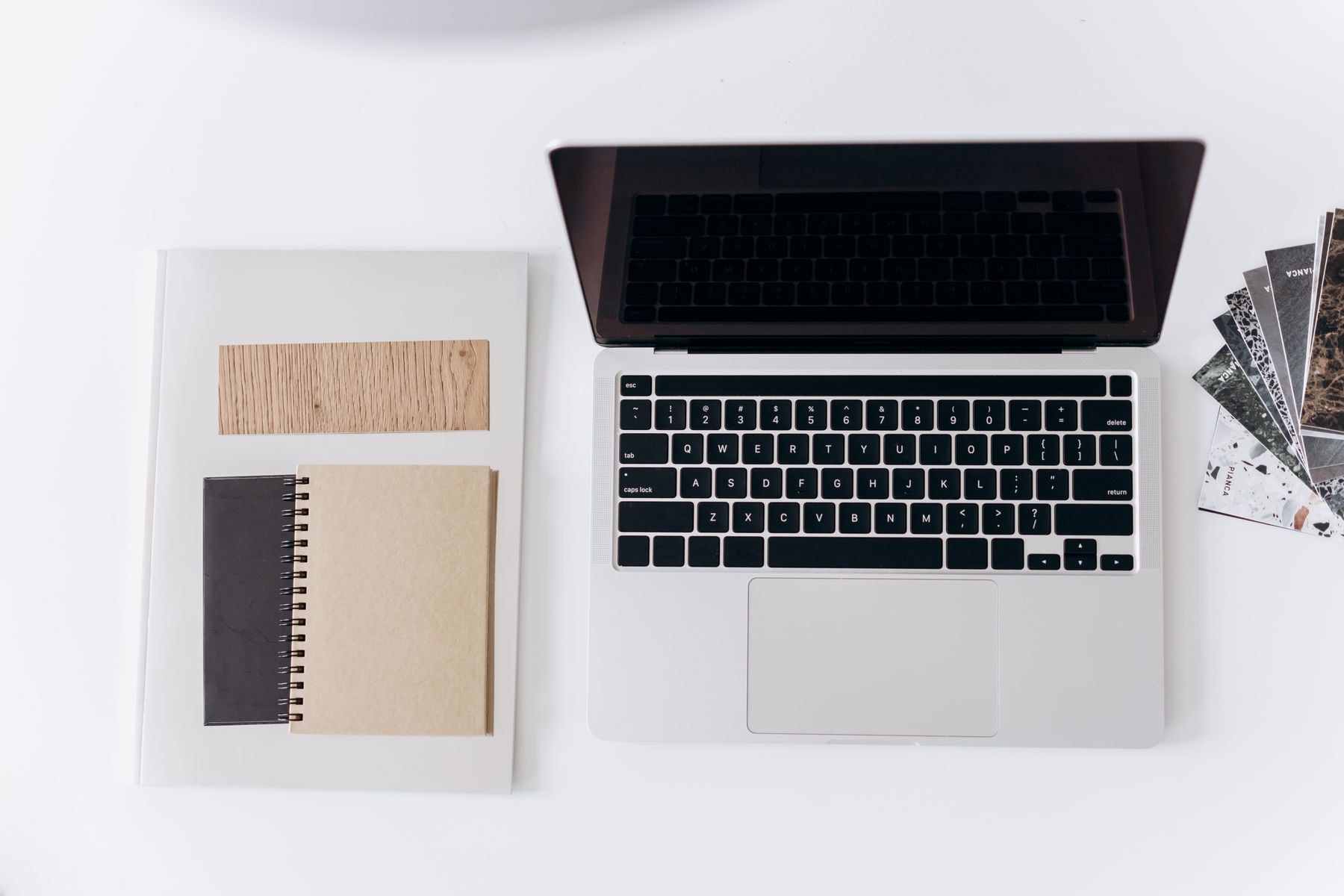 Aufgeräumter Arbeitsplatz mit Laptop, Notizbüchern und Materialmustern